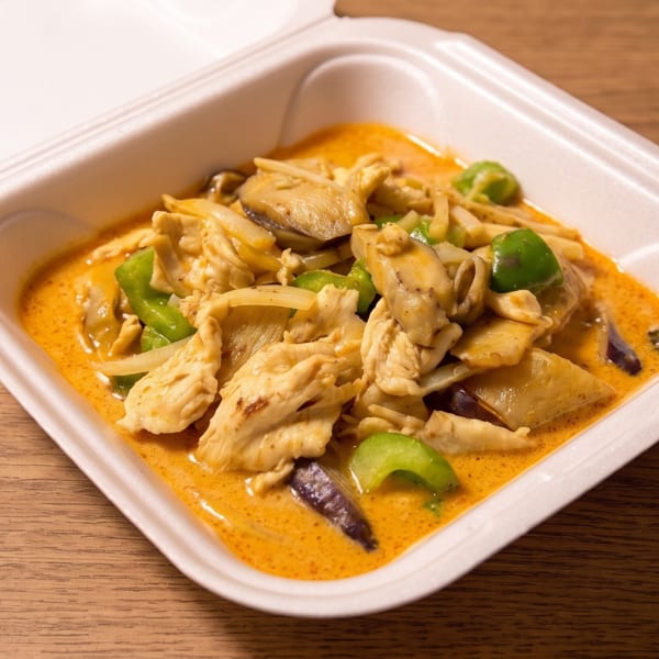 Thai-style chicken curry with eggplant, green peppers, and bamboo shoots in an open takeout container.