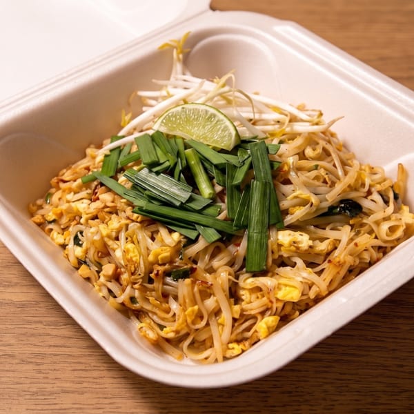 Pad Thai with bean sprouts, scrambled egg, green onions, and lime served in a white takeout container.