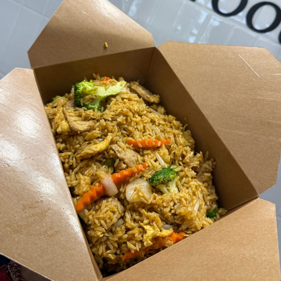 Takeout box filled with fried rice, chicken, scrambled egg, broccoli, carrots, onions, and other mixed vegetables.